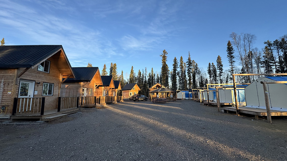 Un plan d’ensemble d’un grand et de cinq petits chalets, d’un pavillon et de cinq tentes autour d’une clairière au cœur d’une forêt.